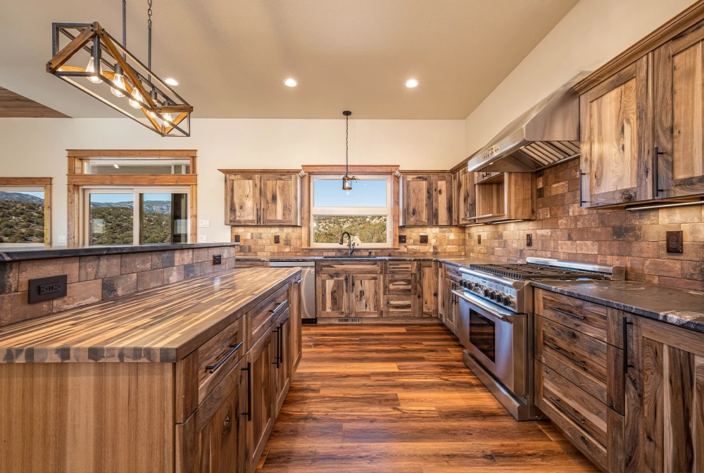 Spacious custom kitchen in a Helton Construction home featuring rich wood cabinetry, a large island with natural stone countertops, hardwood floors, and warm pendant lighting